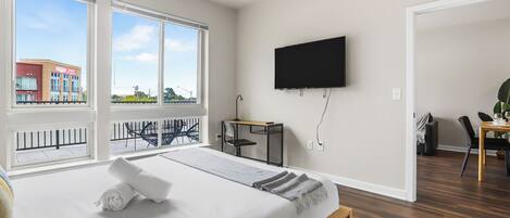 Een moderne hotelkamer met een groot bed, een bureau, een televisie en een balkon met uitzicht op de stad.