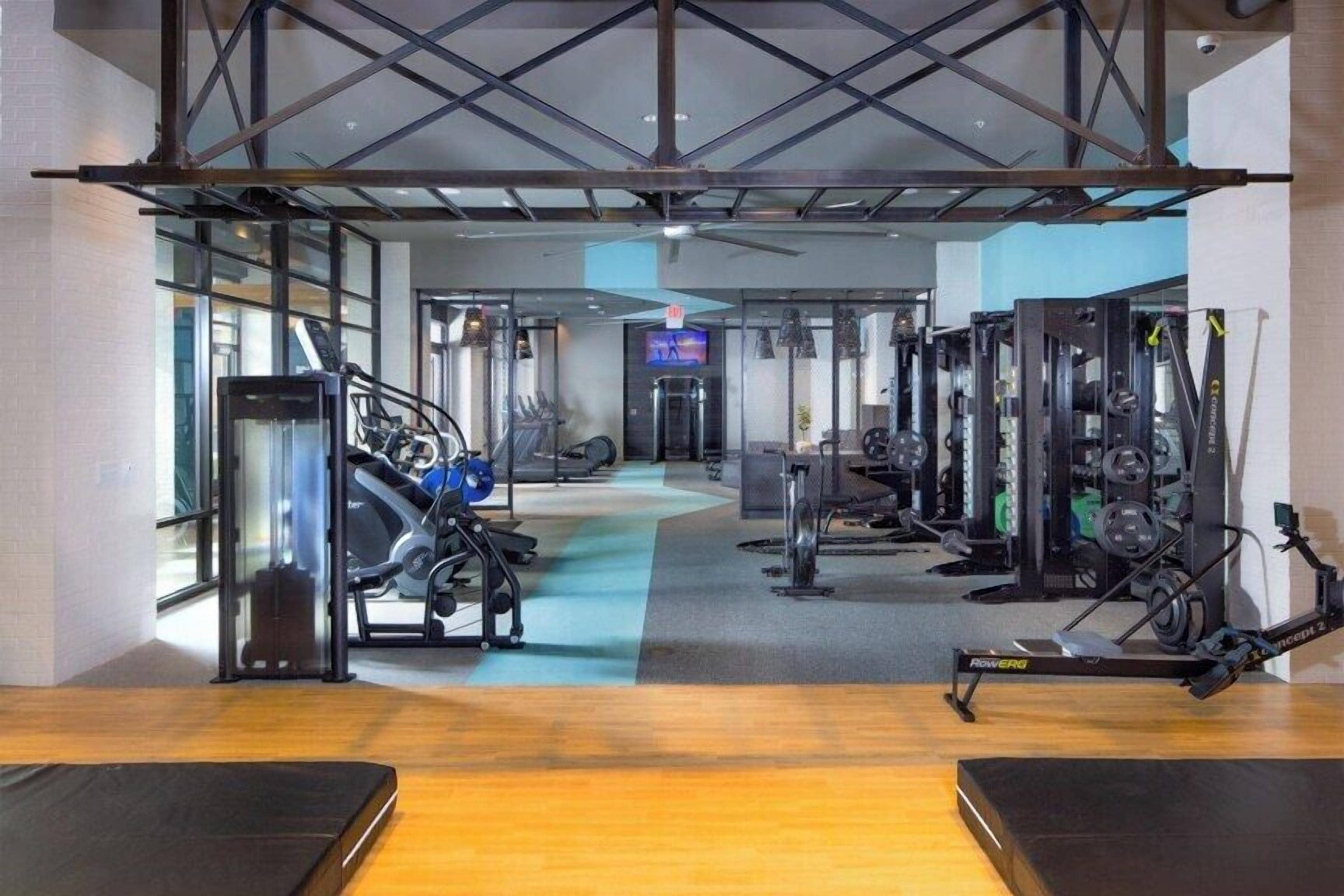 Uma academia com equipamentos de cardio, aparelhos de musculação e um espelho grande na parede.