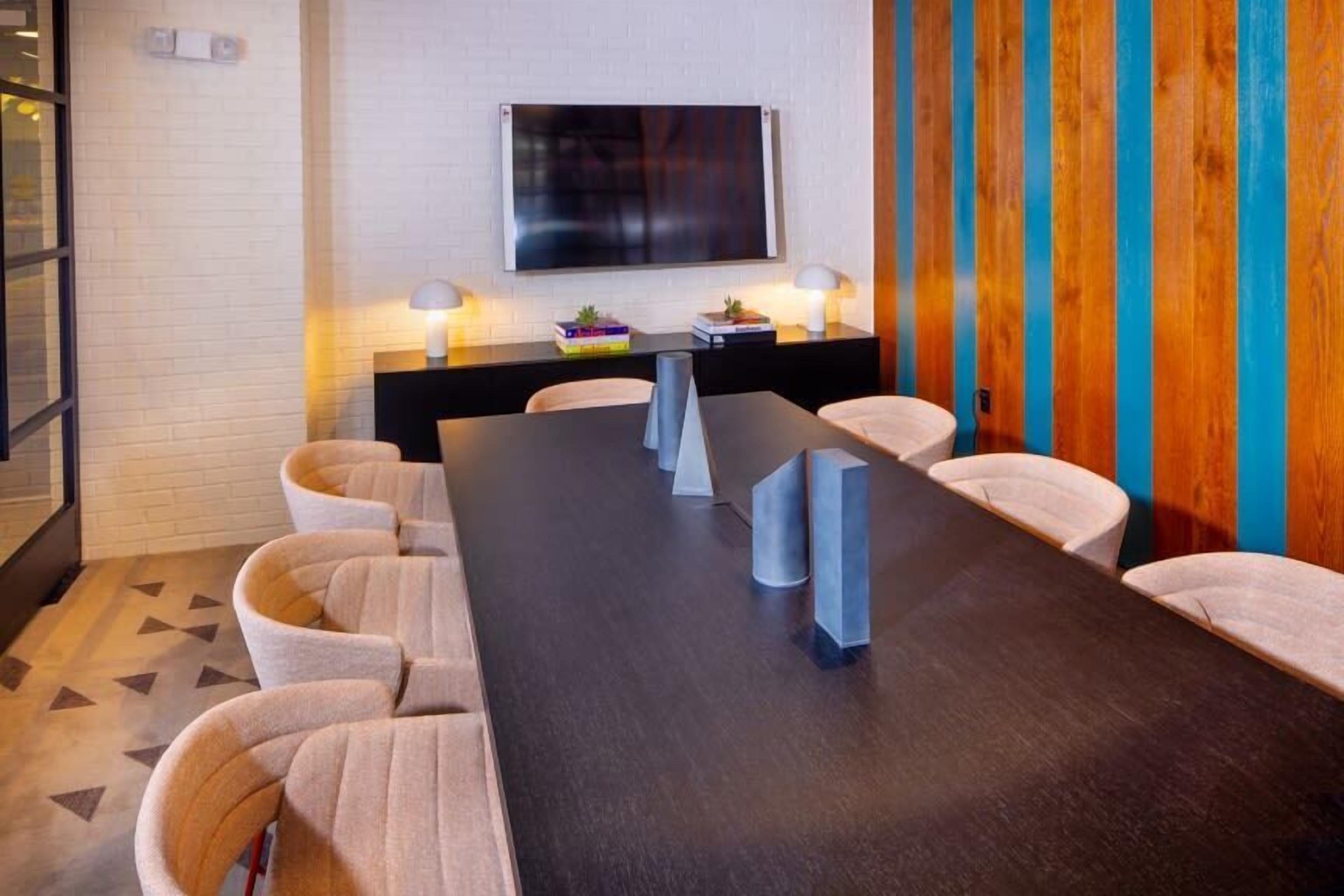 Une salle de conférence avec une longue table, des chaises, un téléviseur fixé au mur et un mur décoratif en bois.