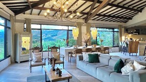 A spacious living area with a high ceiling, large windows, and a view of the outdoors.