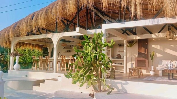 A modern building with a thatched roof, outdoor seating, and a cactus plant.