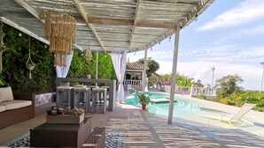 A covered outdoor area with a pool, seating, and a pergola with hanging lights.