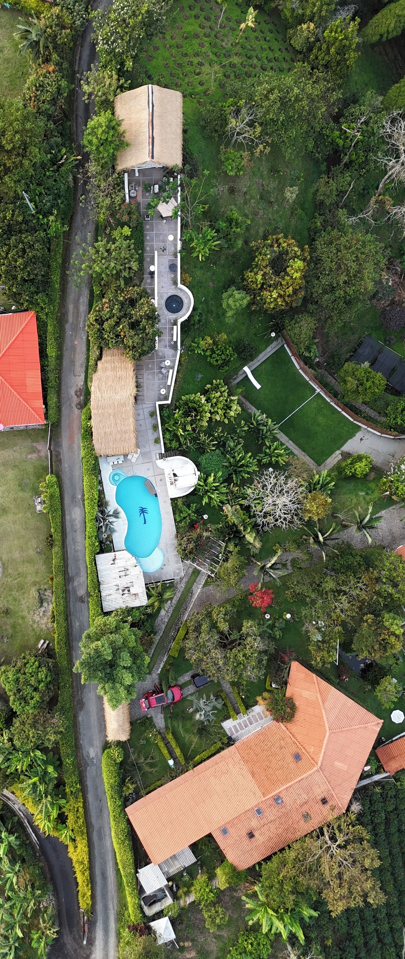Vista aérea de una propiedad con piscina, una estructura de techo de paja y un edificio de techo rojo.
