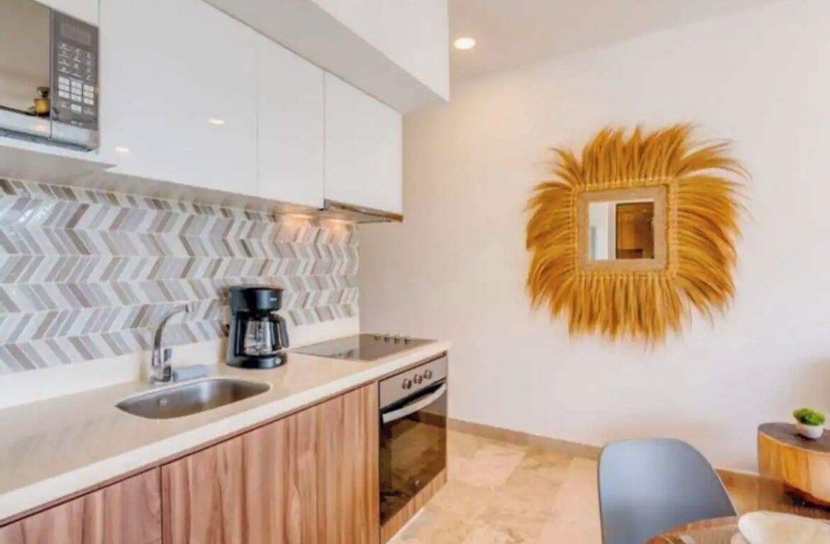 A modern kitchen with a herringbone tile backsplash, a built-in coffee maker, and a wall-mounted decorative mirror.