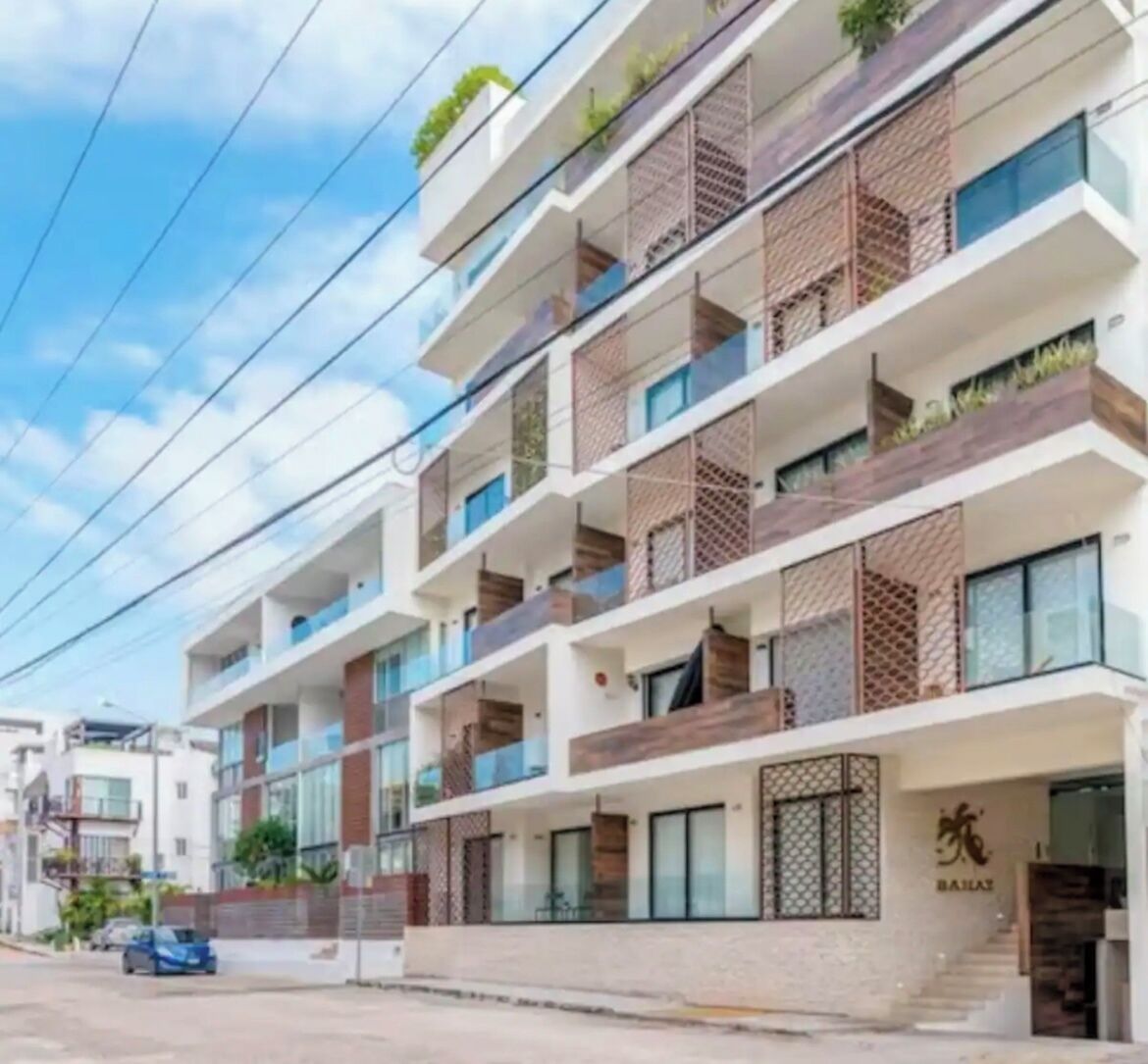 Un hotel de varios pisos con balcones, una entrada visible y un cartel que indica el nombre 'BASILAT'.