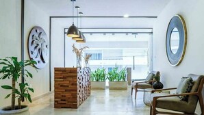 Una moderna zona de recepción con un mostrador de madera, un espejo grande y un espacio de descanso con dos sillones.