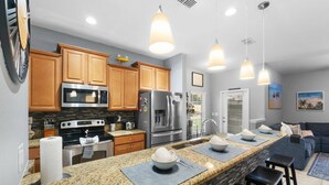 A modern kitchen with granite countertops, stainless steel appliances, wooden cabinets, and pendant lighting. - Zairytale Candy Luxury 5BR, 4BA with Pool in Kissimmee (Kissimmee)