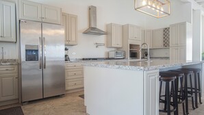A modern kitchen with white cabinetry, stainless steel appliances, a granite countertop, and a bar stool area.