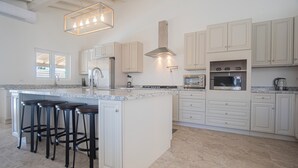 A modern kitchen with white cabinetry, a granite countertop, and a central island with bar stools.