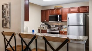 A kitchen with wooden cabinets, a stainless steel refrigerator, a microwave, a stove, and a bar area with wooden chairs. - Spotless Escape in the City`s Core 837 (Clermont)