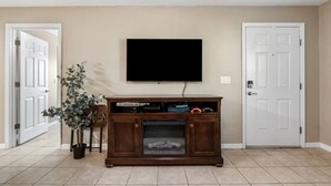 A living room with a flat-screen TV mounted on the wall, a wooden entertainment center with a fireplace, and a potted plant. - Spotless Escape in the City`s Core 837 (Clermont)