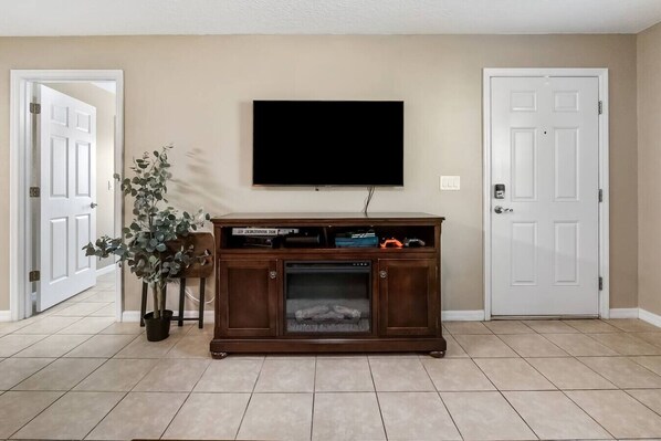Una sala de estar con un televisor de pantalla plana montado en la pared, un mueble de madera con chimenea y una planta en maceta.