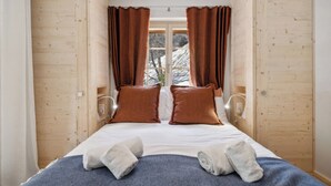 Una habitación con una cama, dos almohadas, una colcha y una ventana con cortinas.