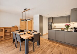 A modern kitchen with grey cabinets, a wooden dining table, and pendant lighting.