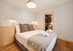 A hotel room with a bed, wooden headboard, bedside lamps, a mirror, and a wooden floor.