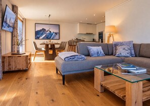 A modern living room with a sofa, a glass coffee table, and a dining area with chairs.