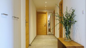 A hallway with a wooden bench, a wooden door at the end, and a vase with flowers on the right. - Luxury Apartment, 3 Bedroom Chalet Rahas A Grimentz - By Mrs Miggins (Grimentz)