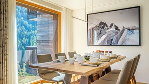 A dining area with a wooden table, chairs, and a large framed picture of mountains. - Luxury Apartment, 3 Bedroom Chalet Rahas A Grimentz - By Mrs Miggins (Grimentz)