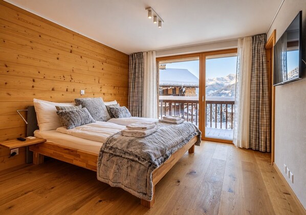 A wooden-paneled bedroom with a bed, a nightstand, and a view of mountains through a glass door.
