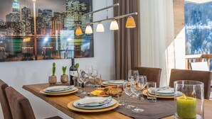 Une table à manger dressée avec des assiettes, des couverts, des verres et une bougie, avec une vue sur le paysage urbain en arrière-plan.