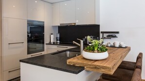 Une cuisine moderne avec des meubles blancs, un plan de travail noir et un îlot central en bois agrémenté d’une plante en pot.