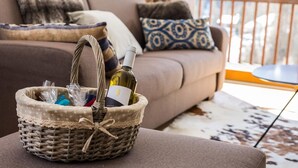 Un panier en osier contenant une bouteille de vin et une carte, posé sur un canapé dans un salon.
