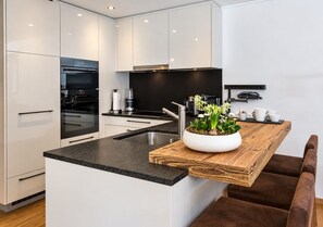 A modern kitchen with white cabinetry, a black countertop, and a wooden island with a plant.