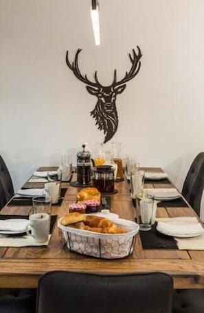 A dining table set with plates, glasses, a coffee pot, and a decorative deer head on the wall.