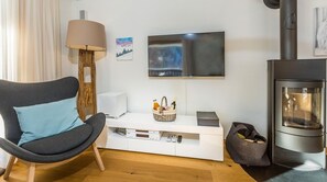 Uma sala de estar moderna com um sofá curvo, televisão de tela plana, lareira e um rack branco com uma luminária e controles remotos.