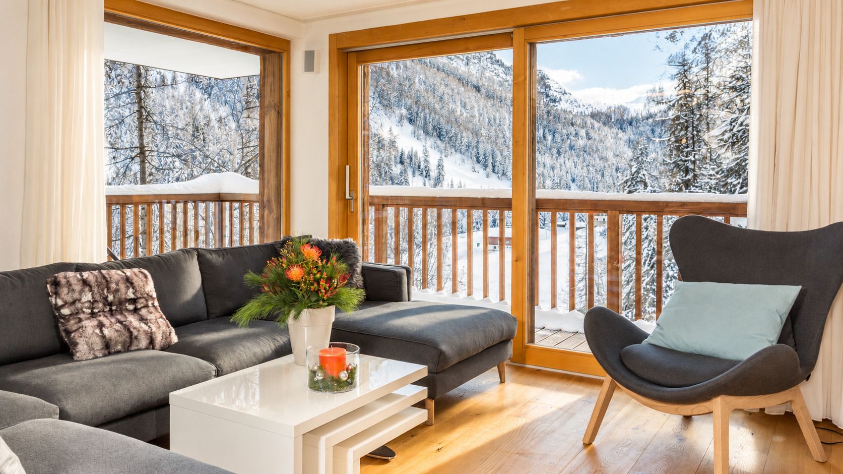 A modern living room with a sofa, armchair, and coffee table, featuring a large window with a snowy mountain view.