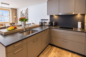 A modern kitchen with a built-in sink, a coffee machine, and a window with a view of snow-covered trees.