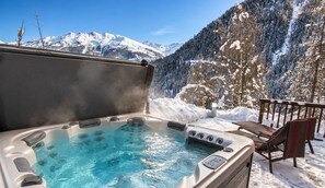 Un jacuzzi con vista a la montaña, rodeado de árboles nevados y una terraza de madera.
