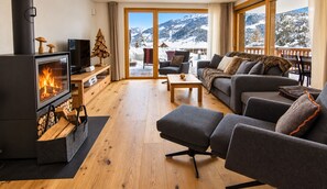 A cozy living room with a fireplace, a sofa, a coffee table, and a view of snowy mountains.
