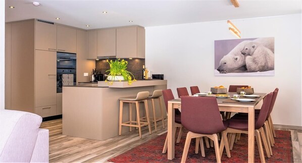 Een moderne keuken met een centraal eiland, houten stoelen en een eettafel voor zes personen.