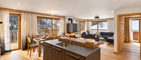 A spacious living area with a large island kitchen, wooden flooring, and a fireplace.