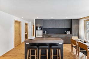 Uma cozinha moderna com uma ilha central, banquetas de bar e uma mesa de jantar com cadeiras.