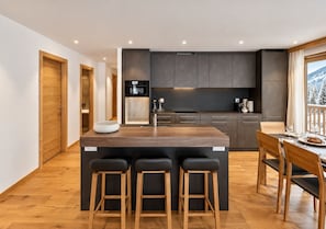 A modern kitchen with a central island, bar stools, and a dining area with a table and chairs.