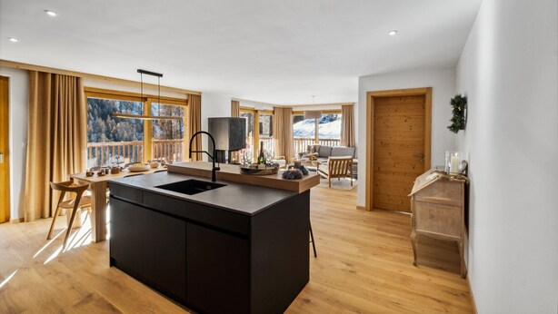 Een moderne keuken met een centraal eiland, houten vloeren en grote ramen met uitzicht op een besneeerd landschap.
