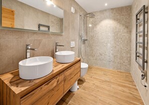 A modern bathroom with two sinks, a shower, and a wooden vanity.