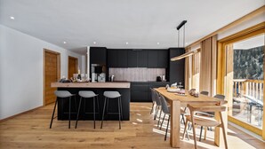 Een moderne keuken met zwarte kastjes, een houten kookeiland met barkrukken, en een eetgedeelte met een houten tafel en stoelen.