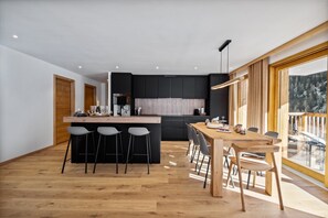 Et moderne køkken med sorte skabe, en træø med barstole og et spiseområde med et træbord og stole.