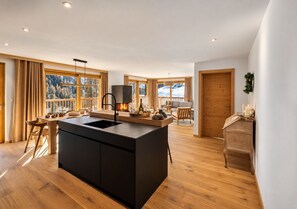 A modern kitchen with a central island, wooden flooring, and large windows offering a view of a snowy landscape.