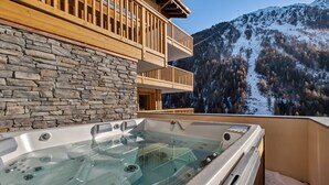 Een stenen muur, een houten balkon en een jacuzzi met uitzicht op de bergen.