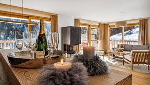 Een gezellige woonkamer met een open haard, een fles champagne, glazen en uitzicht op besneeuwde bergen.