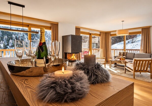 A cozy living room with a fireplace, a bottle of champagne, glasses, and a candle on a wooden table.