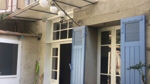 A patio with a glass-top table and chairs, a blue shuttered window, and a white door. - Maison de Village, en Provence Dans Triangle Avignon-arlesnîmes (Vallabrègues)