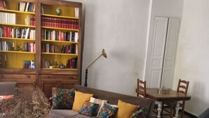 A cozy living room with a checkered floor, a bookshelf, a sofa with colorful cushions, and a dining table with chairs. - Maison de Village, en Provence Dans Triangle Avignon-arlesnîmes (Vallabrègues)