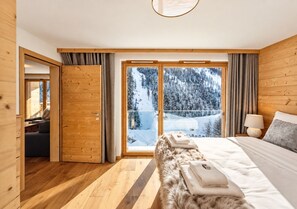 Ett sovrum med ett stort fönster, träväggar, en säng och utsikt över ett snötäckt landskap.
