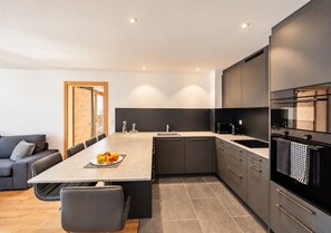 A modern kitchen with a central island, dark cabinetry, and a dining area with a sofa and chairs.
