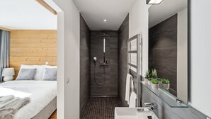 Un baño moderno con cabina de ducha de vidrio, un espejo grande y una mesita de noche con lámpara.